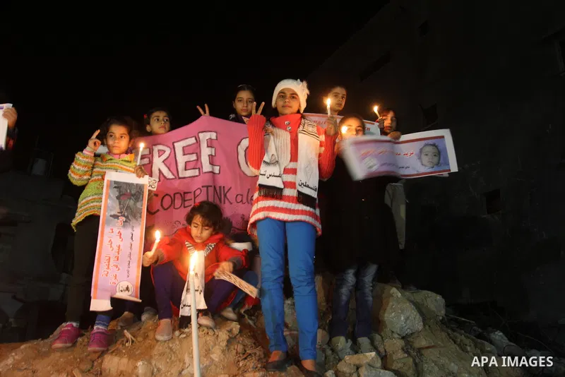Palestinian childrens hold candles during a solidarity march with the Dalu family next to their house, as well as a wrecked car festooned with candles, which was hit by an Israeli strike during Israel's recent military o...