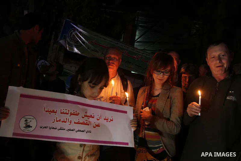 Palestinian and foreign activists hold candles during a solidarity march with the Dalu family next to their house, as well as a wrecked car festooned with candles, which was hit by an Israeli strike during Israel's recen...