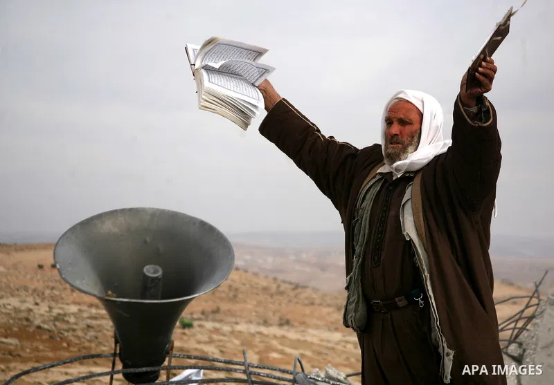 A Palestinian man holds copies of the Koran as he stands near the speaker of a mosque that was demolished by Israeli forces in the West Bank village of al-Mufaqara, south of Hebron, on December 04, 2012. Photo by Mamoun...