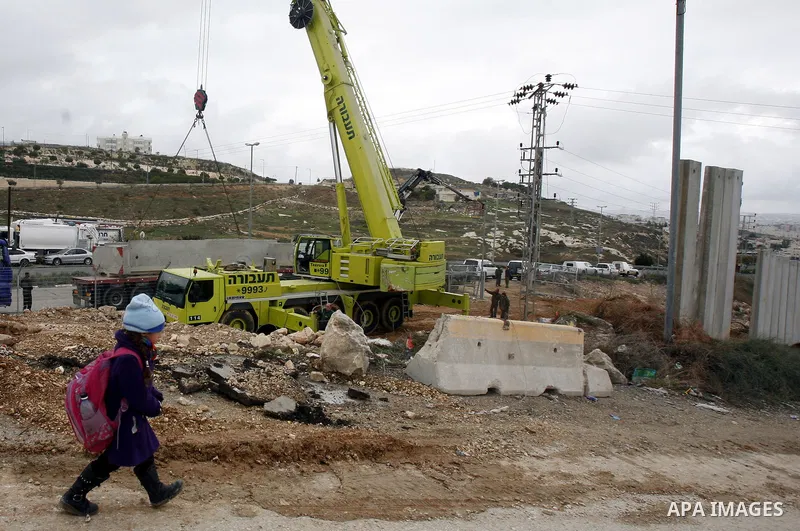 A Palestinian schoolgirl walks while Israeli laborers install concrete sections during the the construction of the separation barrier wall in the Palestinian neighborhood of Shuafat in East Jerusalem, 05 Dec, 2012. Photo...