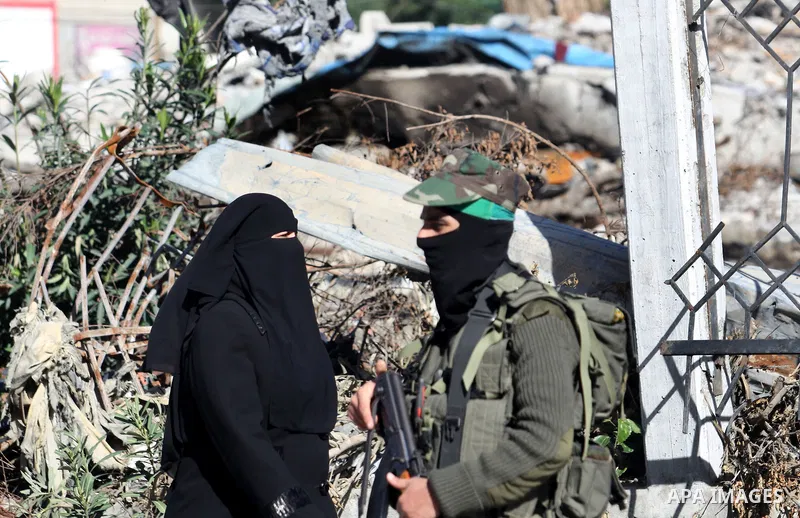 A Palestinian woman walk pass a member of the Ezzedine al-Qassam brigade, the armed wing Hamas, as they prepare for the arrival of the Islamist movement's exiled politburo chief Khaled Meshaal who is due in the Gaza Stri...