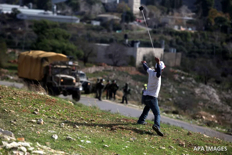 A Palestinian protester uses a slingshot to throw stones from the roof of a house during clashes following a demonstration against the expropriation of Palestinian land by Israel in the West Bank village of Nabi Saleh on...