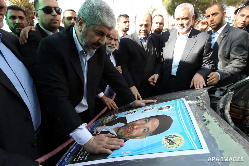 Hamas chief Khaled Meshaal (2nd L) prays beside a poster depicting late Hamas military commander Ahmed Al-Jaabari which pasted on the remains of the car that he was riding in when he was killed in an Israeli air strike,...