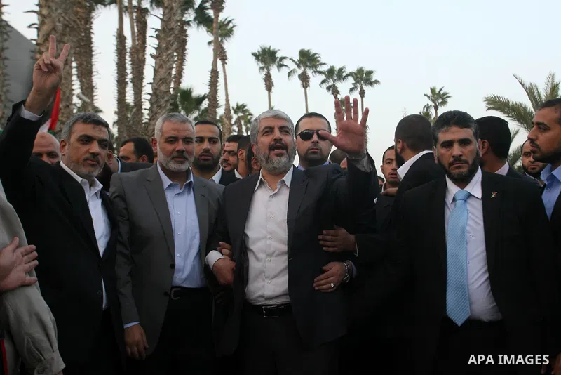 Hamas leader in exile Khaled Meshaal waves goodbye while standing next to Palestinian Prime Minister in the Gaza Strip Ismail Haniya and Hamas leader Izzat al-Rishq, upon his departure from the Gaza Strip on December 10,...