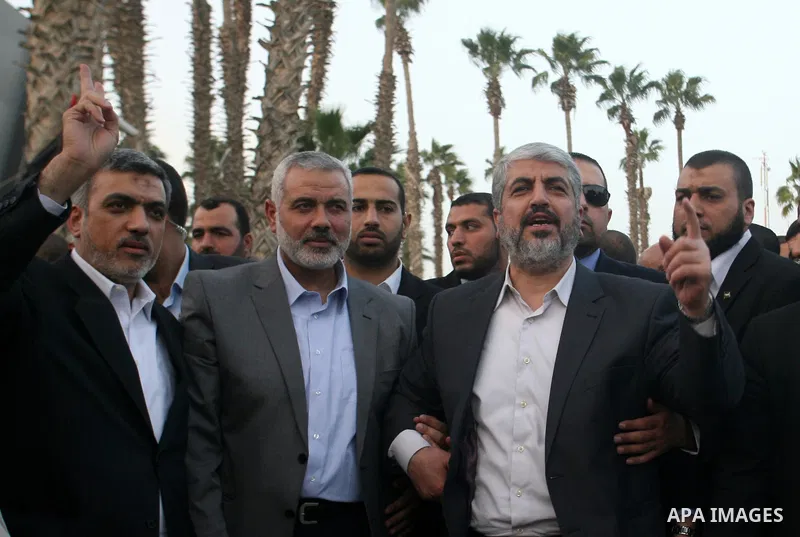 Hamas leader in exile Khaled Meshaal waves goodbye while standing next to Palestinian Prime Minister in the Gaza Strip Ismail Haniya and Hamas leader Izzat al-Rishq, upon his departure from the Gaza Strip on December 10,...