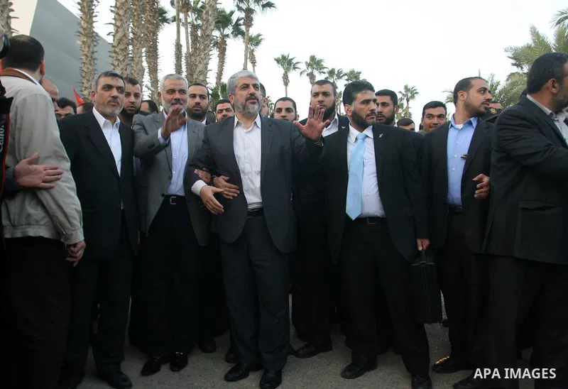 Hamas leader in exile Khaled Meshaal waves goodbye while standing next to Palestinian Prime Minister in the Gaza Strip Ismail Haniya and Hamas leader Izzat al-Rishq, upon his departure from the Gaza Strip on December 10,...