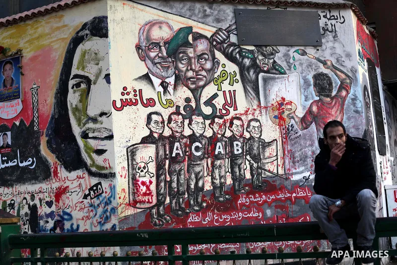 A Egyptian sits at the presidential palace and anti-Morsi graffiti is seen on the palace's wall behind him in Cairo, Dec. 18, 2012. Egypt's opposition staged rallies across the country on Tuesday to protest against the d...