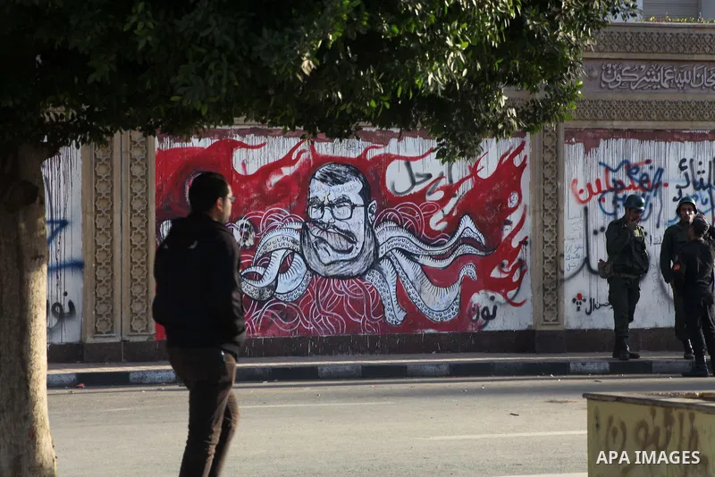 Egyptians opposition supporter stand at the presidential palace and anti-Morsi graffiti is seen on the palace's wall behind him in Cairo, Dec. 18, 2012. Egypt's opposition staged rallies across the country on Tuesday to...