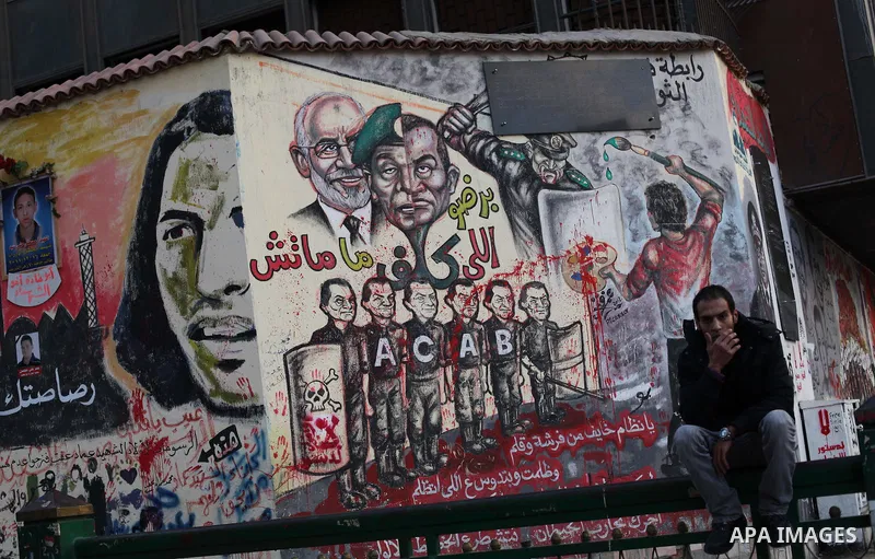 A Egyptian sits at the presidential palace and anti-Morsi graffiti is seen on the palace's wall behind him in Cairo, Dec. 18, 2012. Egypt's opposition staged rallies across the country on Tuesday to protest against the d...