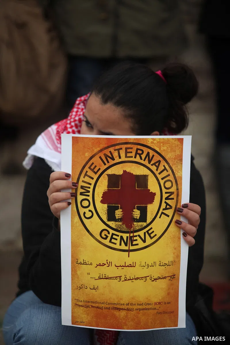 Palestinian protesters hold posters and a sign reading "ICRC, do your work or leave" during a demonstration in support of Palestinian prisoners held in Israeli jails, some of whom are observing a hunger strike, outside t...