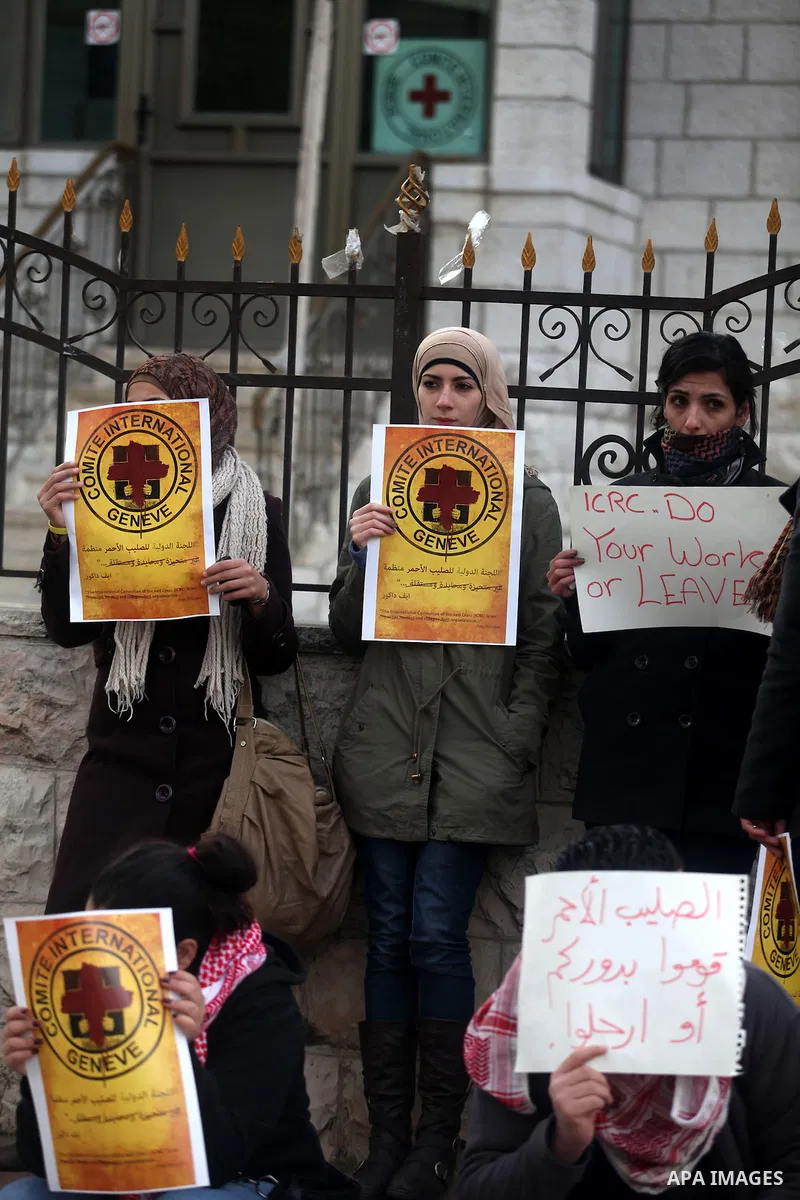 Palestinian protesters hold posters and a sign reading "ICRC, do your work or leave" during a demonstration in support of Palestinian prisoners held in Israeli jails, some of whom are observing a hunger strike, outside t...