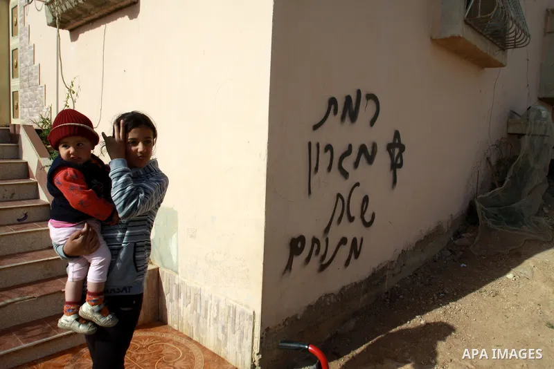 Palestinian children stand next a wall with text read in Hebrow 'Migron' and 'battlefield' in the village of Majdal Bani Fadel, near the West Bank City of Nablus, 20 December 2012. According to Palestinian security offic...