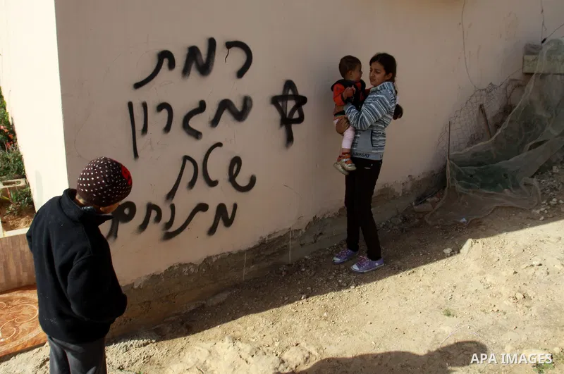 Palestinian children stand next a wall with text read in Hebrow 'Migron' and 'battlefield' in the village of Majdal Bani Fadel, near the West Bank City of Nablus, 20 December 2012. According to Palestinian security offic...