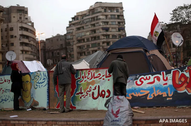 People stand in front of a graffiti at Tahrir Square where protesters opposing President Mohamed Mursi are camping in Cairo December 20, 2012. Egyptian Islamist groups are planning a mass protest in Alexandria on Friday,...