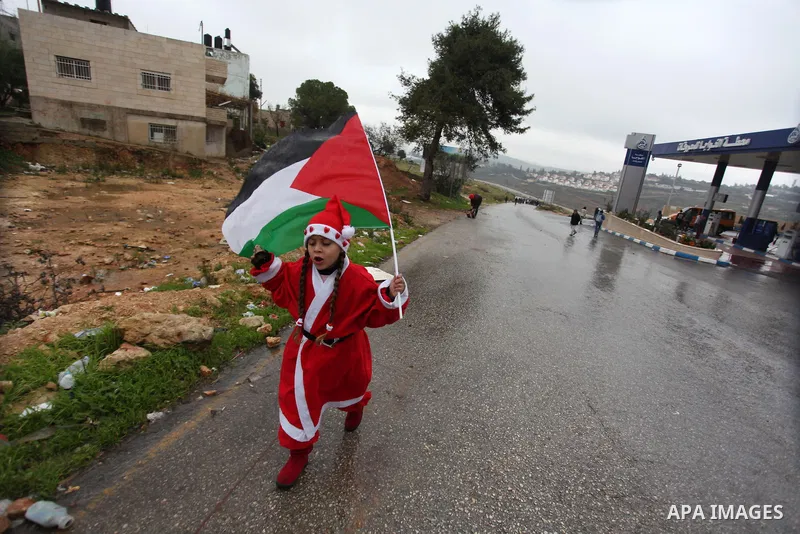 A Palestinian girl dressed as Pope Claus and holds national flag during a weekly protest against the Jewish settlement of Halamish in the West Bank village of Nabi Saleh, near Ramallah December 21, 2012. Photo by Issam R...