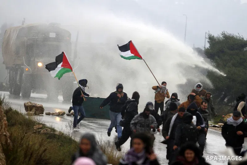 Palestinian protesters run as an Israeli Army truck fires a water cannon, containing a foul-smelling substance, during clashes with stone-throwing protesters in the West Bank village of Nabi Saleh, near Ramallah December...