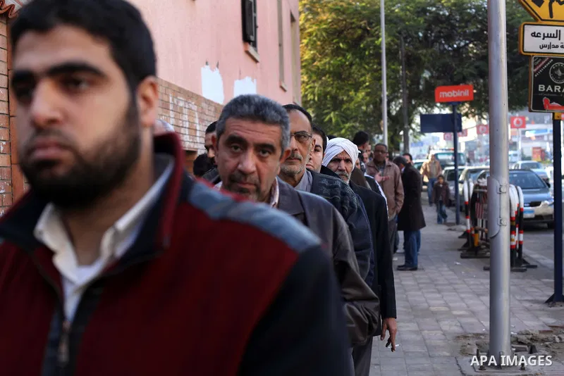 Egyptian men queue with other voters at a polling station during the second round of a referendum on a new draft constitution in Giza, south of Cairo, on December 22, 2012. Egyptians are voting in the final round of a re...