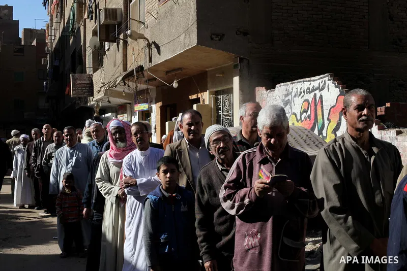 Egyptian men queue with other voters at a polling station during the second round of a referendum on a new draft constitution in Giza, south of Cairo, on December 22, 2012. Egyptians are voting in the final round of a re...