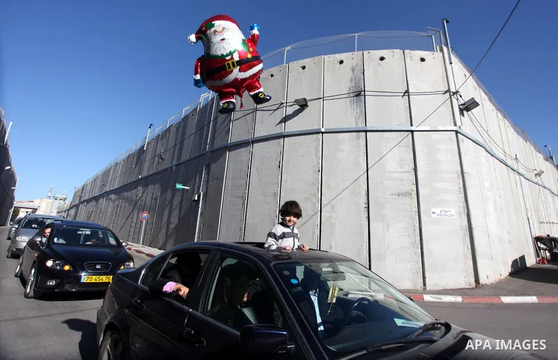 A Palestinian boy holds a Santa Claus balloon as a convey of cars transporting the Latin Patriarch of Jerusalem Fouad Twal cross through an Israeli checkpoint to the West Bank city of Bethlehem December 24, 2012. Twal cr...