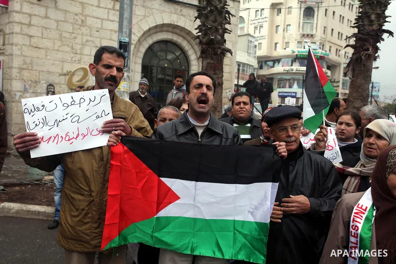 Palestinians hold placards and their national flags during a demonstration in the West Bank city of Ramallah calling for an end in the political division and commitment to the reconciliation agreement between rival Pales...