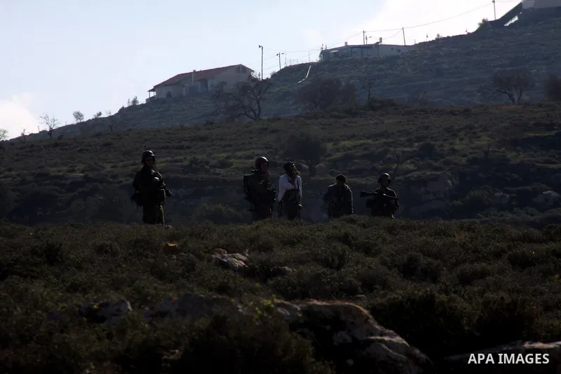 Israeli soldiers stand guard next to Israeli settlers from the Yetshar settlement after they attacked Palestinian farmers from the West Bank village of Qusra near the West Bank City of Nablus 27 December 2012. Photo by N...