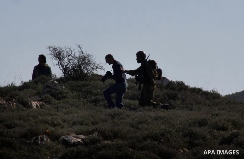 An Israeli soldier stops a settler from he Yetshar settlement after settlers attacked Palestinian farmers from the West Bank village of Qusra near the West Bank City of Nablus 27 December 2012. Photo by Nedal Eshtayah