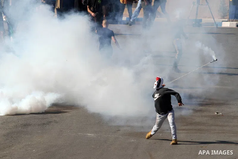 A Palestinian stone-throwing protester uses a sling to throw back a tear gas canister fired by Israeli security officers (unseen) during clashes at a protest against Jewish settlements, in the West Bank village of Nabi S...