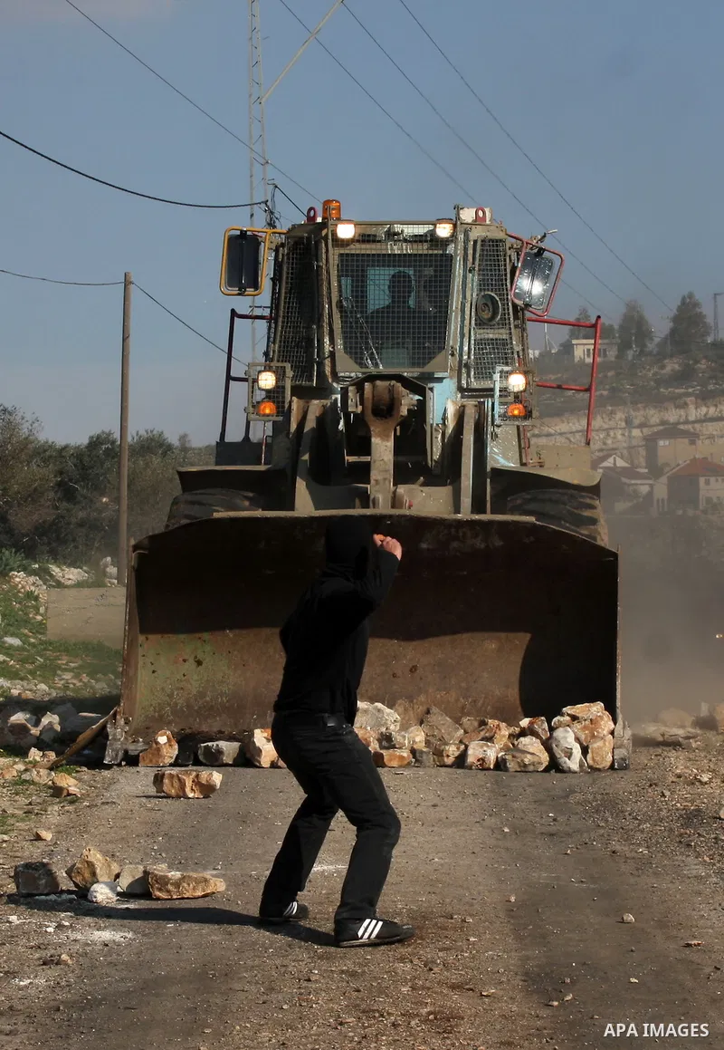 A Palestinian demonstrator throws stones at an Israeli bulldozer during clashes at the weekly protest against the Jewish settlement of Qadomem, near Nablus, West Bank, 28 December 2012. According to Palestinian sources,...