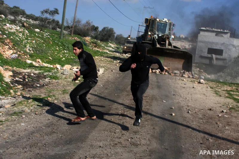 Palestinian demonstrators throw stones at an Israeli bulldozer during clashes at the weekly protest against the Jewish settlement of Qadomem, near Nablus, West Bank, 28 December 2012. According to Palestinian sources, fi...