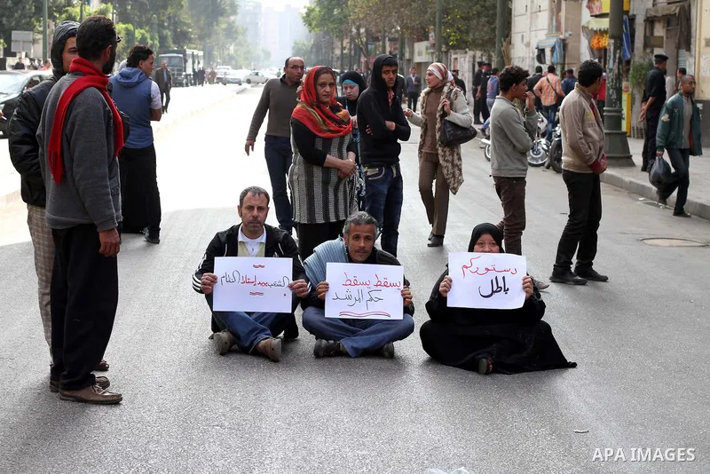protesters holding signs, and sit in front of police officers near the Shura Council, the upper house of parliament where the Constituent Assembly drafted the country's new constitution, as protesters against Egypt's Pre...