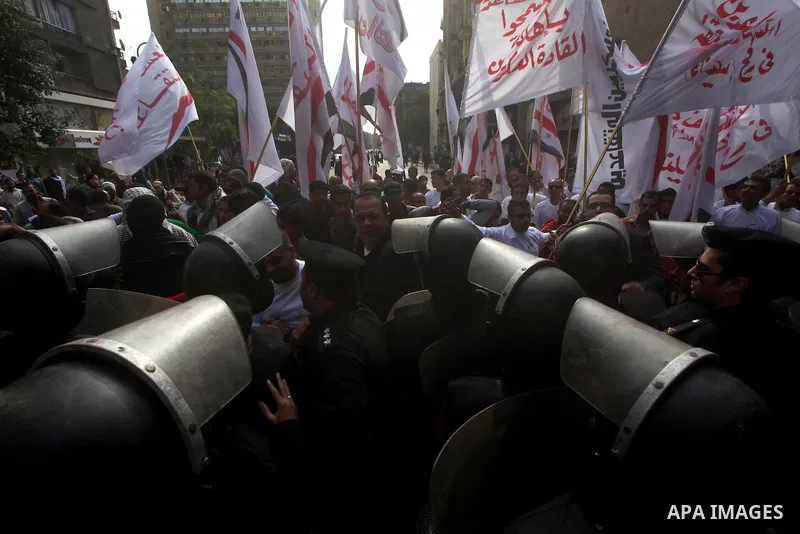 protesters holding signs, in front of police officers near the Shura Council, the upper house of parliament where the Constituent Assembly drafted the country's new constitution, as protesters against Egypt's President M...