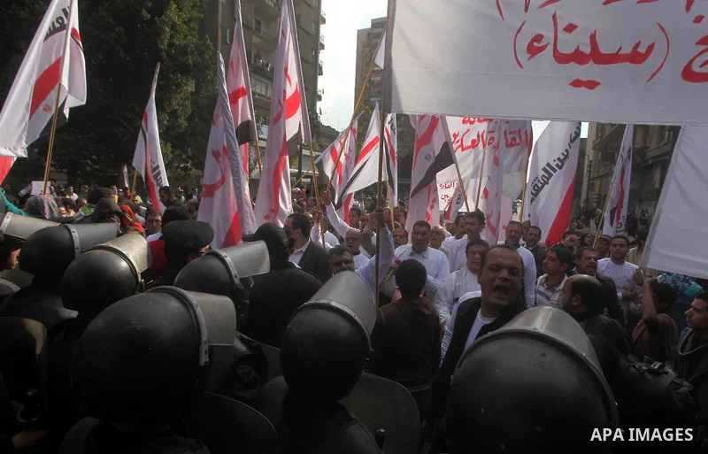 protesters holding signs, in front of police officers near the Shura Council, the upper house of parliament where the Constituent Assembly drafted the country's new constitution, as protesters against Egypt's President M...