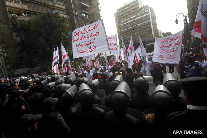 protesters holding signs, in front of police officers near the Shura Council, the upper house of parliament where the Constituent Assembly drafted the country's new constitution, as protesters against Egypt's President M...