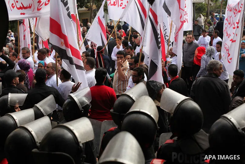 protesters holding signs, in front of police officers near the Shura Council, the upper house of parliament where the Constituent Assembly drafted the country's new constitution, as protesters against Egypt's President M...