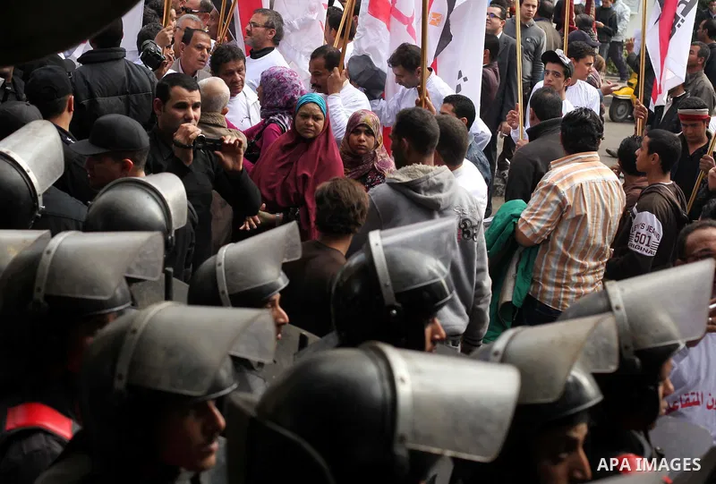 protesters holding signs, in front of police officers near the Shura Council, the upper house of parliament where the Constituent Assembly drafted the country's new constitution, as protesters against Egypt's President M...