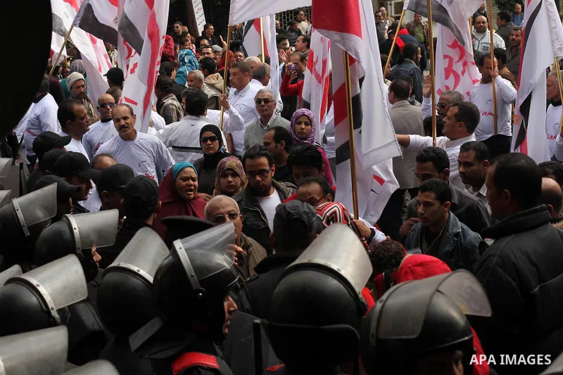 protesters holding signs, in front of police officers near the Shura Council, the upper house of parliament where the Constituent Assembly drafted the country's new constitution, as protesters against Egypt's President M...