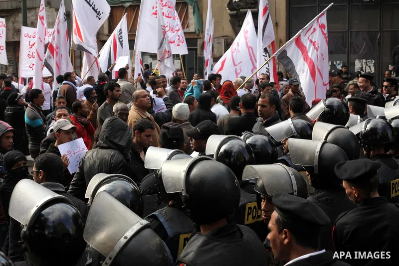 protesters holding signs, in front of police officers near the Shura Council, the upper house of parliament where the Constituent Assembly drafted the country's new constitution, as protesters against Egypt's President M...