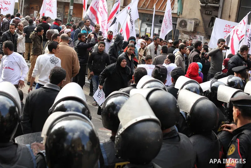 protesters holding signs, in front of police officers near the Shura Council, the upper house of parliament where the Constituent Assembly drafted the country's new constitution, as protesters against Egypt's President M...
