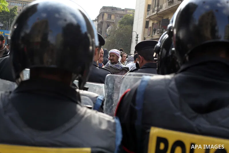 protesters holding signs, in front of police officers near the Shura Council, the upper house of parliament where the Constituent Assembly drafted the country's new constitution, as protesters against Egypt's President M...