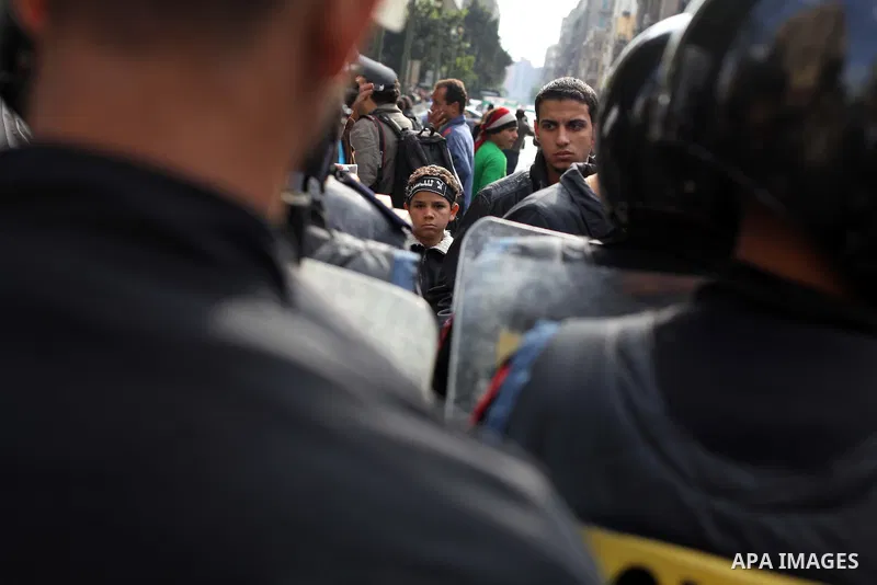 protesters holding signs, in front of police officers near the Shura Council, the upper house of parliament where the Constituent Assembly drafted the country's new constitution, as protesters against Egypt's President M...