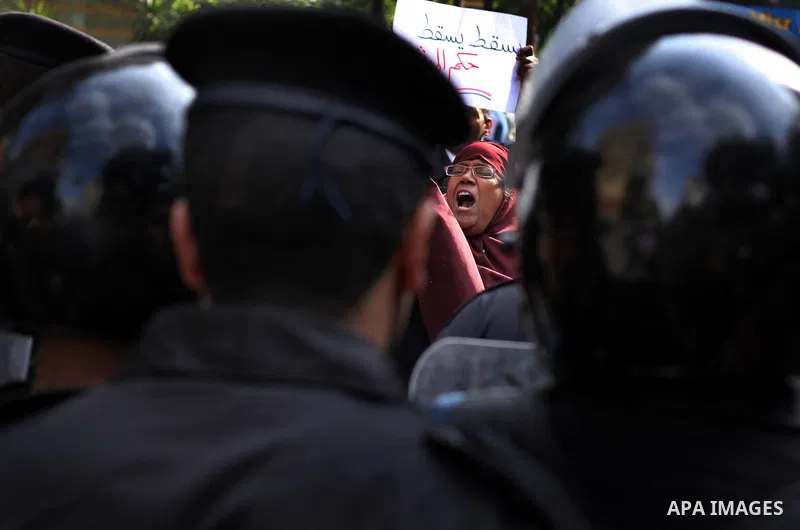 protesters holding signs, in front of police officers near the Shura Council, the upper house of parliament where the Constituent Assembly drafted the country's new constitution, as protesters against Egypt's President M...