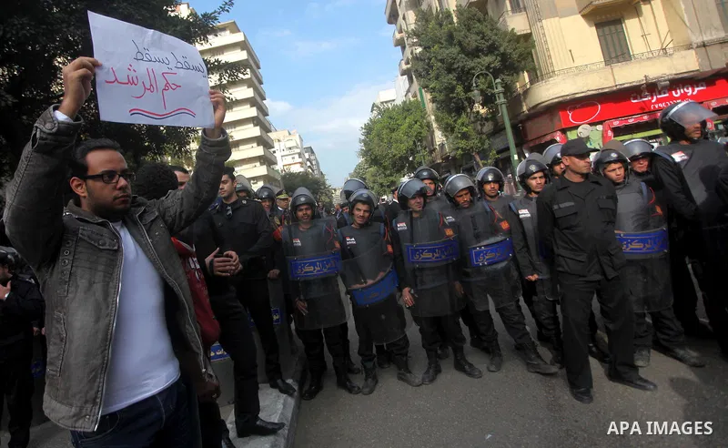 protesters holding signs, in front of police officers near the Shura Council, the upper house of parliament where the Constituent Assembly drafted the country's new constitution, as protesters against Egypt's President M...