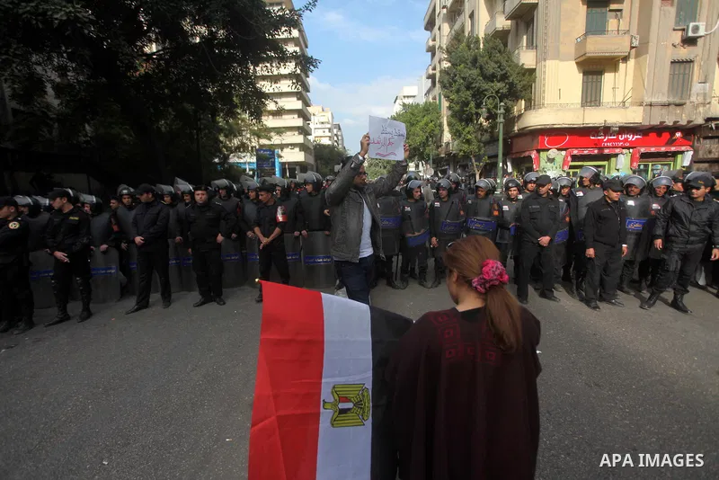 protesters holding signs, in front of police officers near the Shura Council, the upper house of parliament where the Constituent Assembly drafted the country's new constitution, as protesters against Egypt's President M...