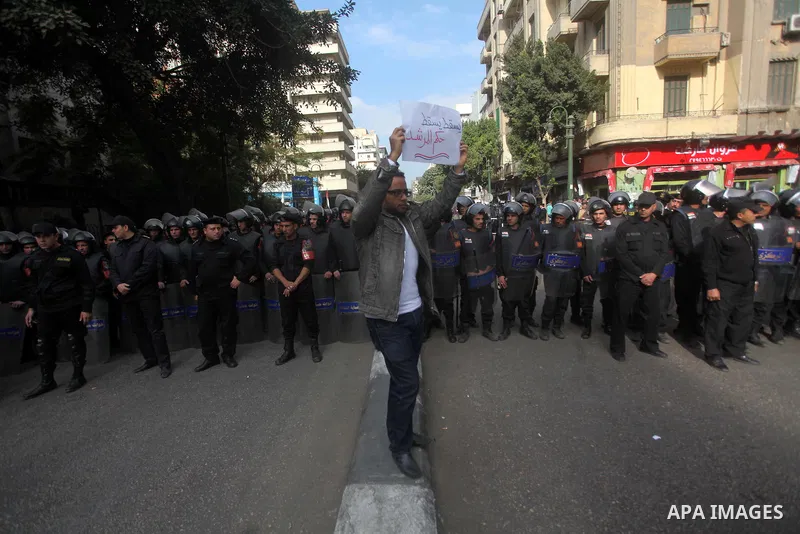 protesters holding signs, in front of police officers near the Shura Council, the upper house of parliament where the Constituent Assembly drafted the country's new constitution, as protesters against Egypt's President M...