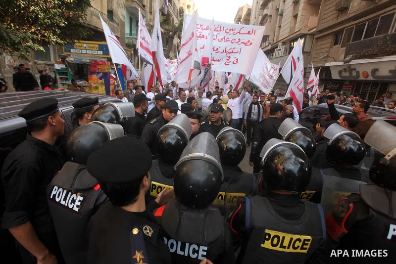 protesters holding signs, in front of police officers near the Shura Council, the upper house of parliament where the Constituent Assembly drafted the country's new constitution, as protesters against Egypt's President M...