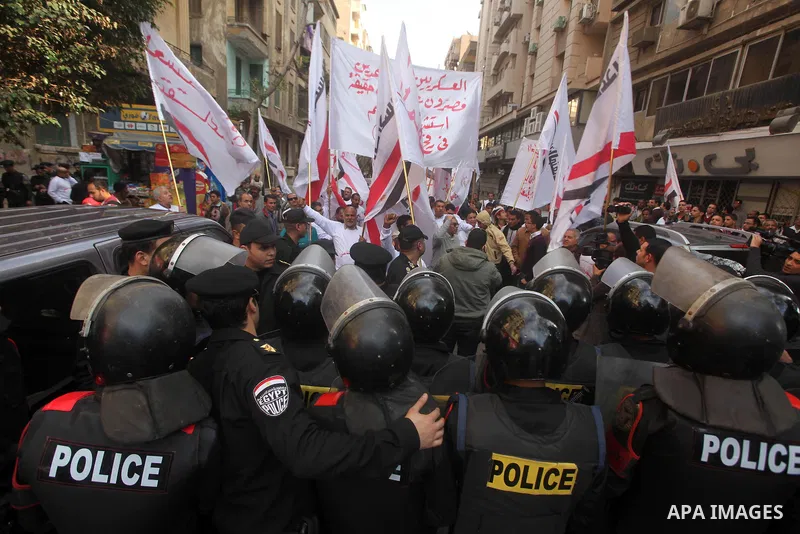 protesters holding signs, in front of police officers near the Shura Council, the upper house of parliament where the Constituent Assembly drafted the country's new constitution, as protesters against Egypt's President M...