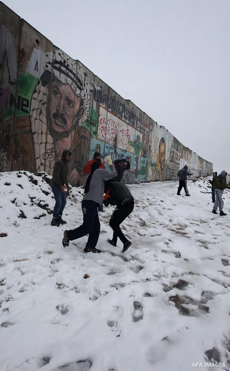 Palestinians play in the snow next to a section of Israel's separation barrier in Qalandia between Jerusalem and the West bank city of Ramallah, Thursday, Jan. 10, 2013. Stormy weather conditions continued on Thursday wi...