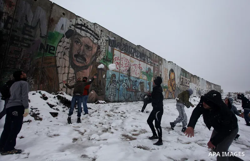 Palestinians play in the snow next to a section of Israel's separation barrier in Qalandia between Jerusalem and the West bank city of Ramallah, Thursday, Jan. 10, 2013. Stormy weather conditions continued on Thursday wi...