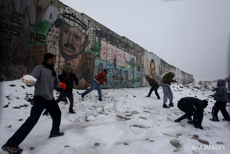 Palestinians play in the snow next to a section of Israel's separation barrier in Qalandia between Jerusalem and the West bank city of Ramallah, Thursday, Jan. 10, 2013. Stormy weather conditions continued on Thursday wi...