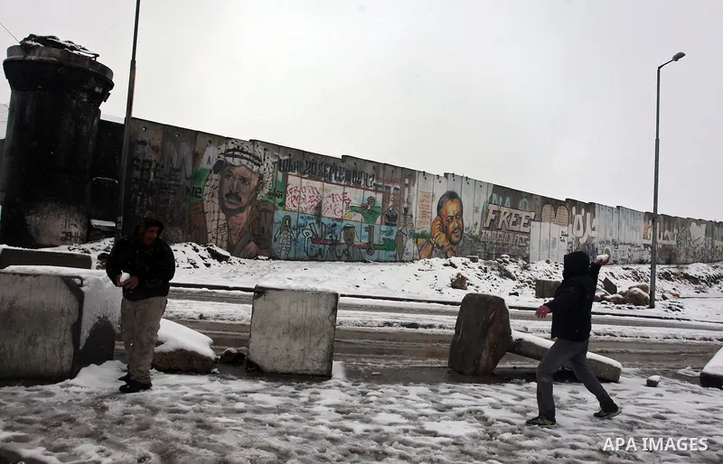 Palestinians play in the snow next to a section of Israel's separation barrier in Qalandia between Jerusalem and the West bank city of Ramallah, Thursday, Jan. 10, 2013. Stormy weather conditions continued on Thursday wi...